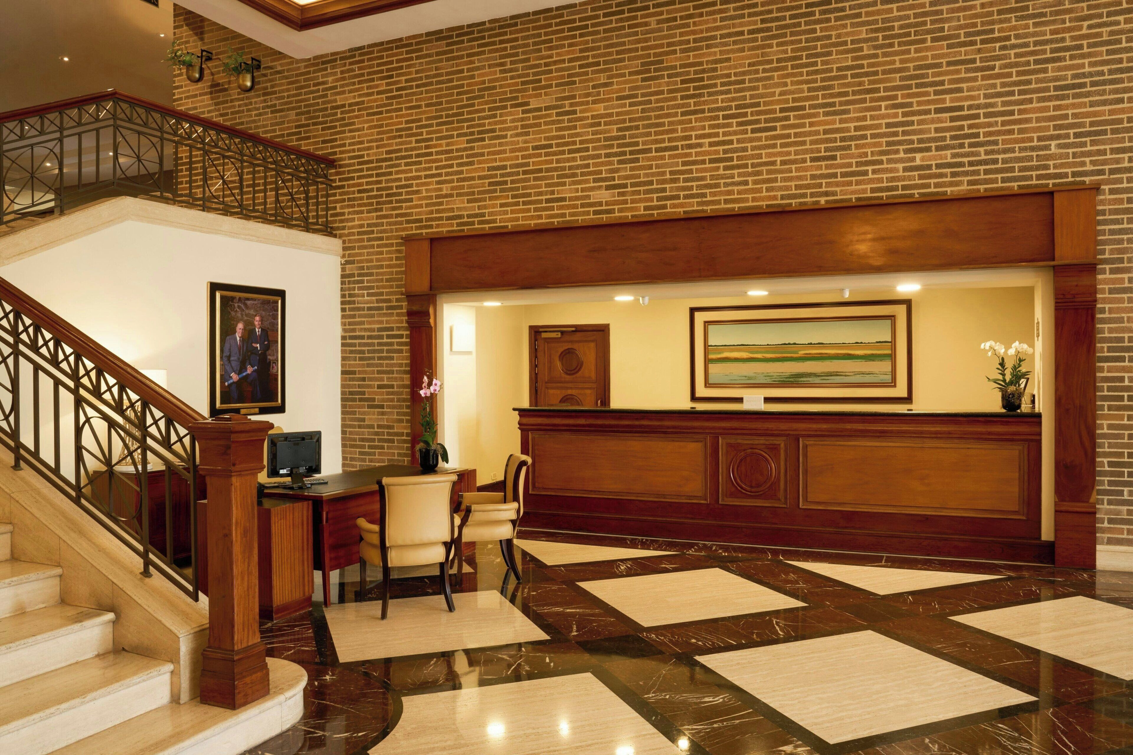 A reception area with a wooden reception desk, a framed painting above it, and a staircase with a metal railing leading to an upper level.