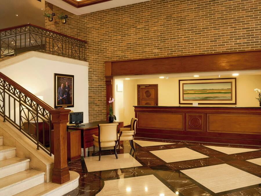 A reception area with a wooden reception desk, a framed painting above it, and a staircase with a metal railing leading to an upper level.