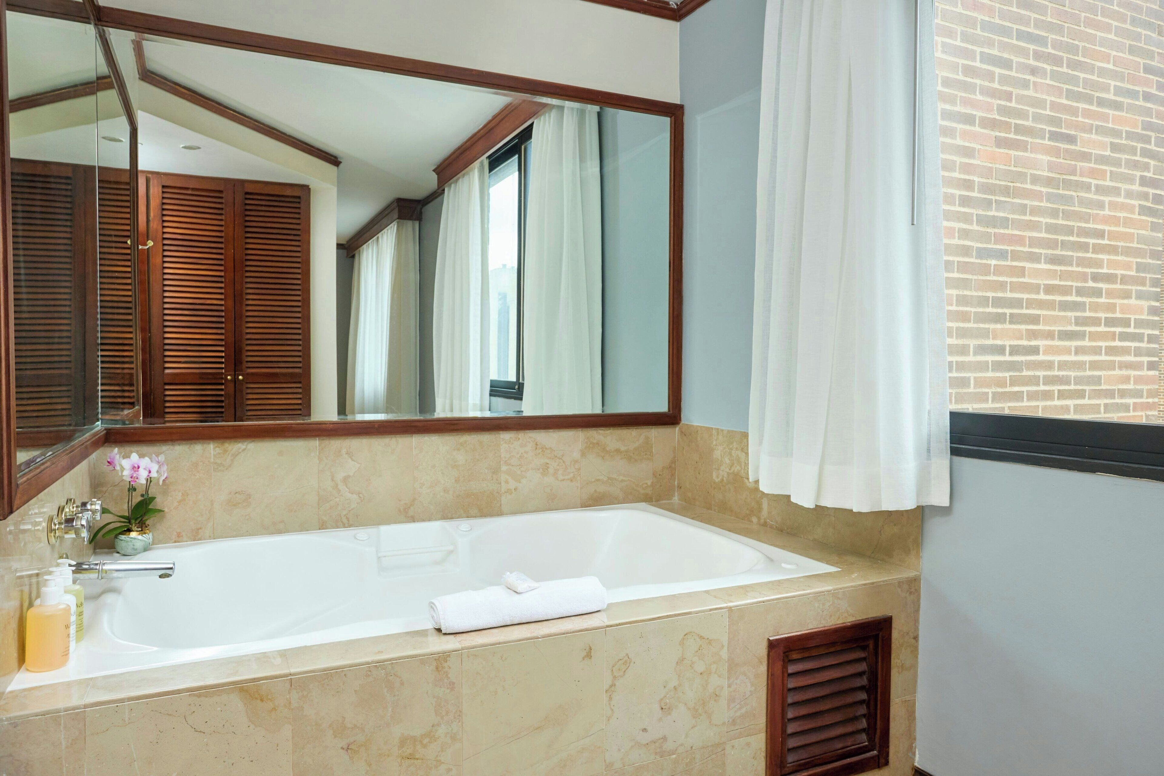 A bathroom with a large mirror, a bathtub, and a window with curtains.