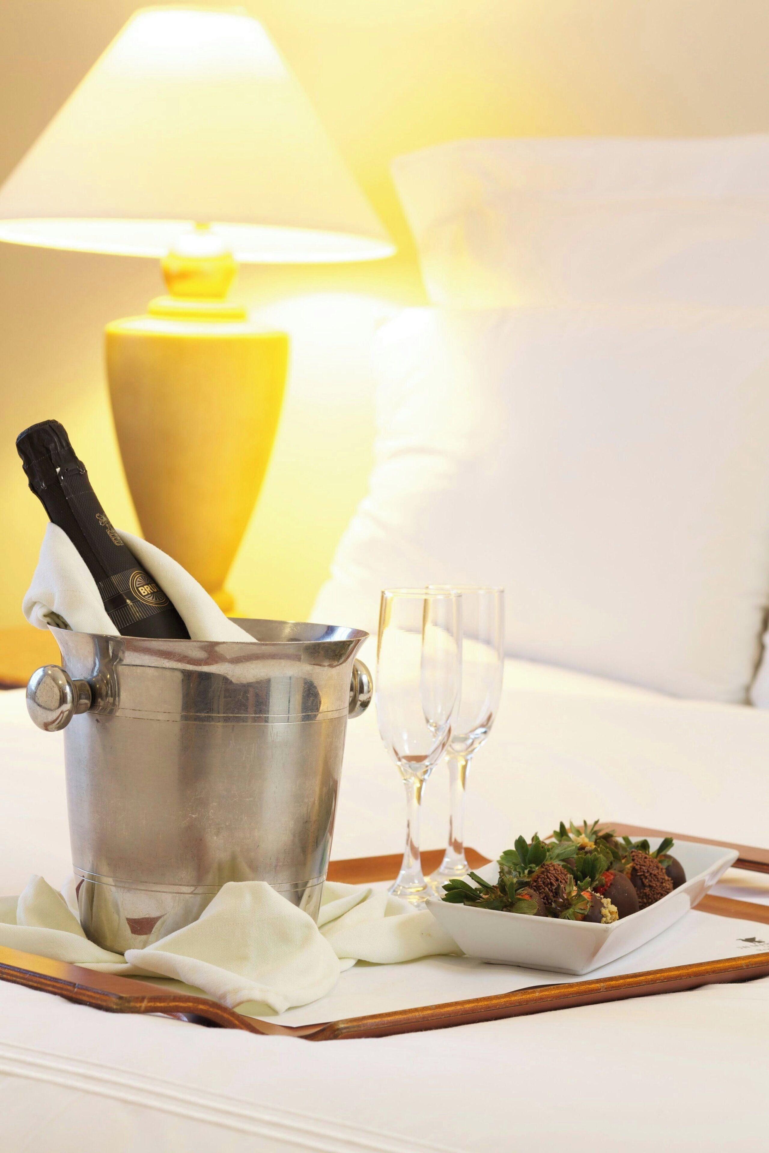 A metal bucket with a bottle of champagne, two empty glasses, and a plate of food on a tray.