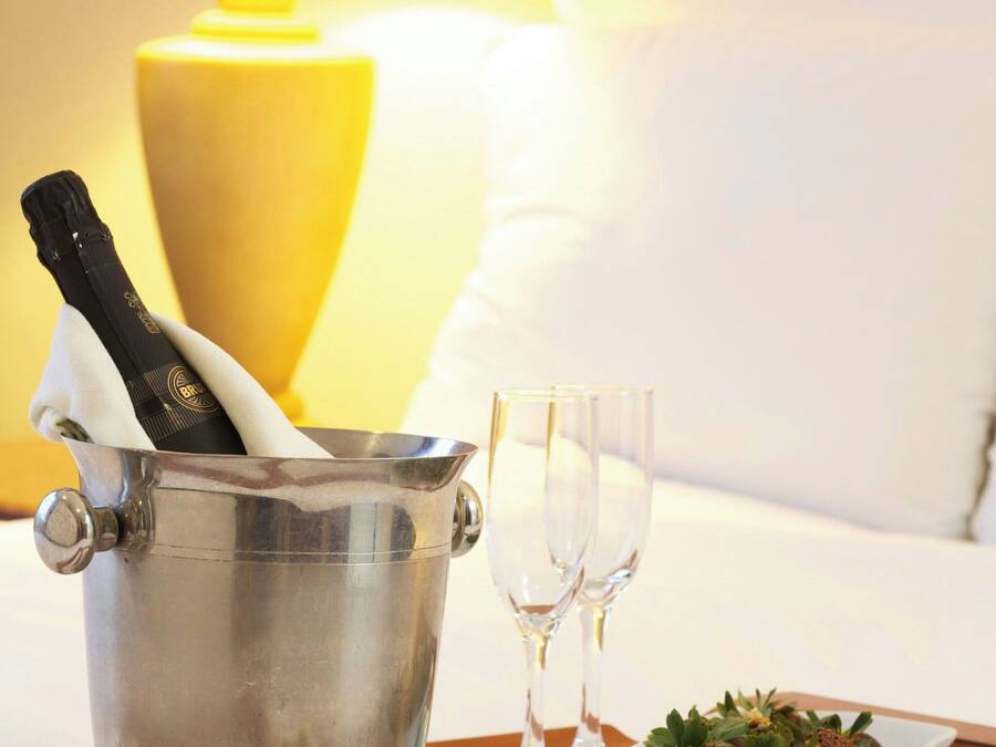 Un balde de metal con una botella de champán, dos copas vacías y un plato de comida sobre una bandeja.