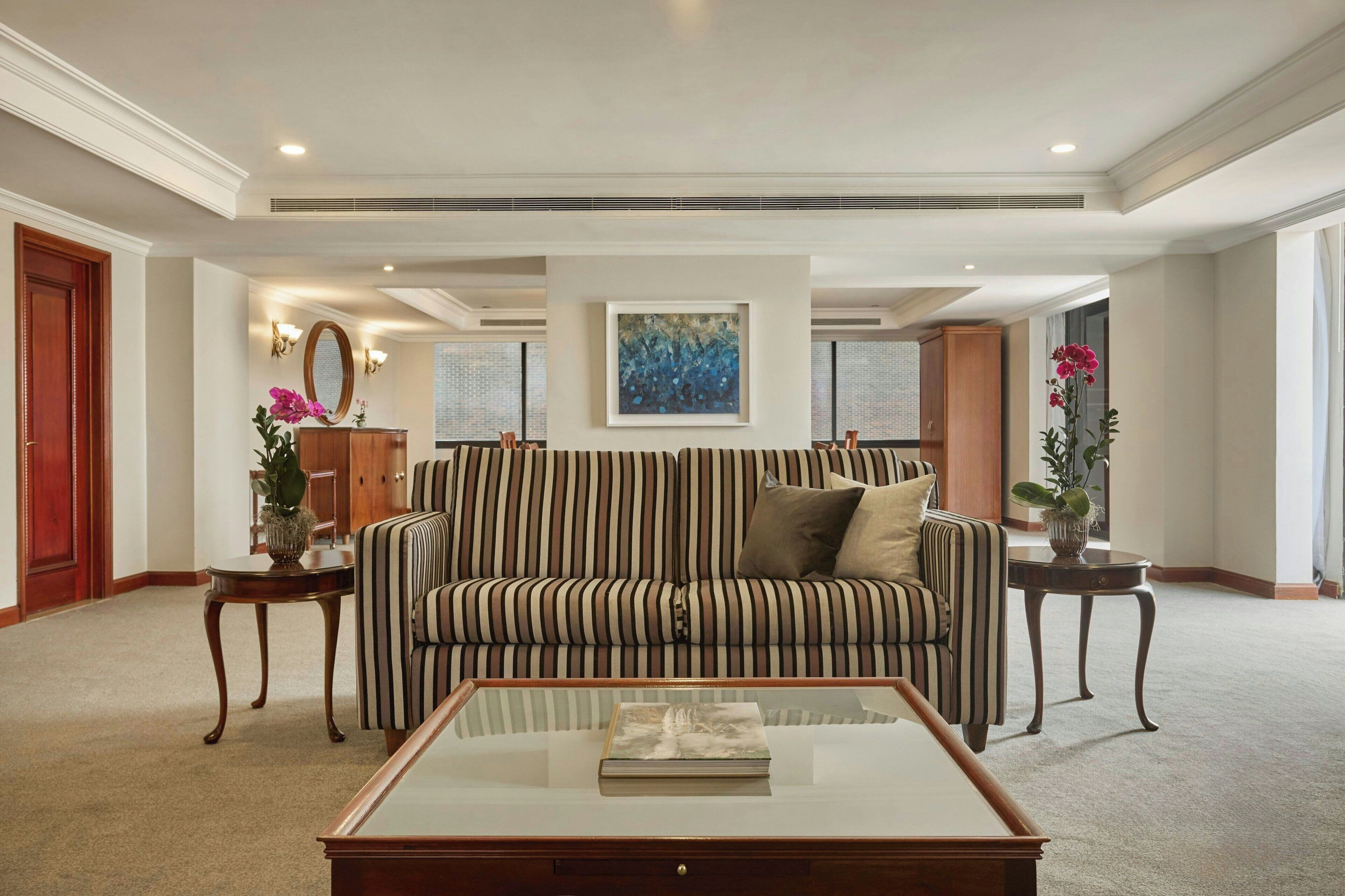 A living room with a striped sofa, a glass coffee table, and decorative plants.