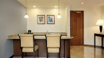 A kitchen with a bar area, two chairs, a wooden door, and a table with a lamp.