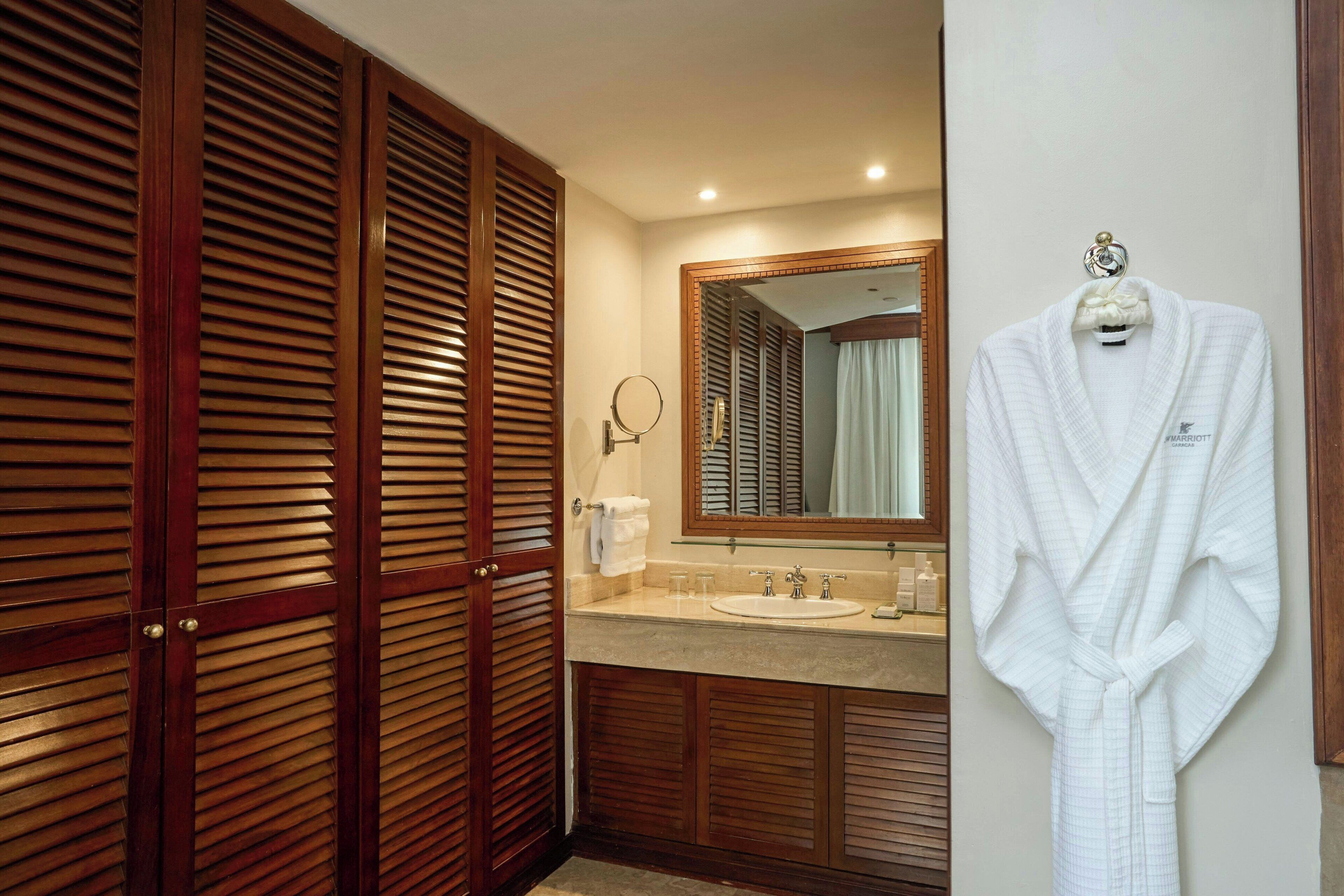 A hotel bathroom with a wooden vanity, a sink, a mirror, and a robe hanging on the wall.