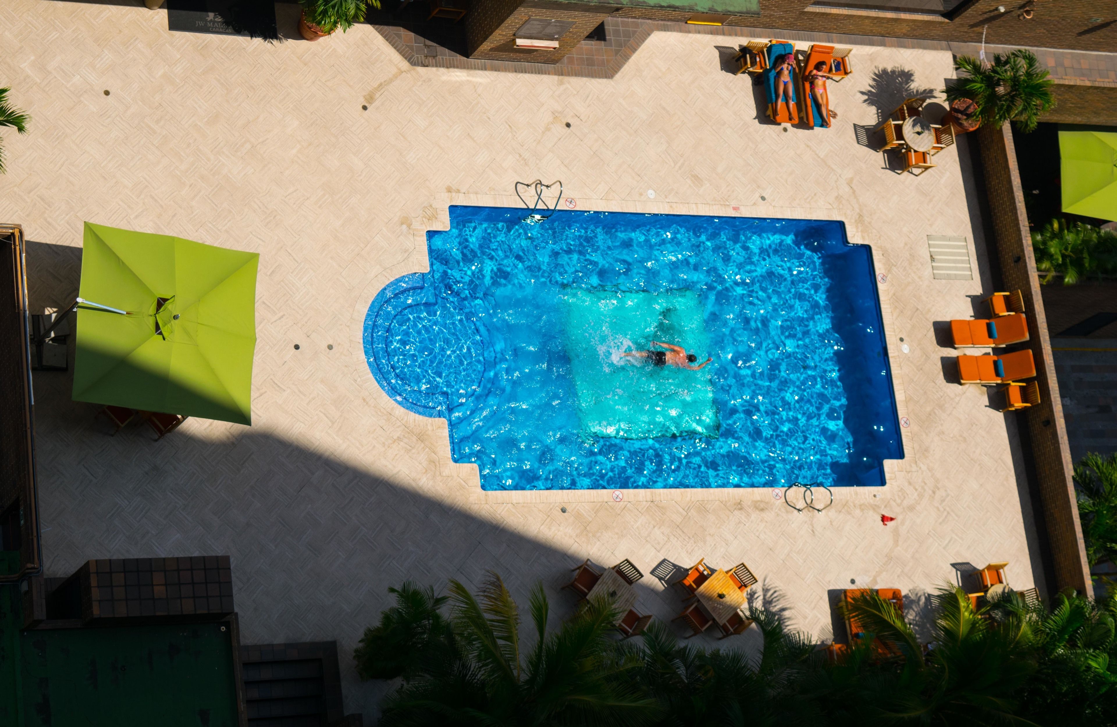 A rooftop pool with a swimmer, surrounded by lounge chairs and umbrellas.