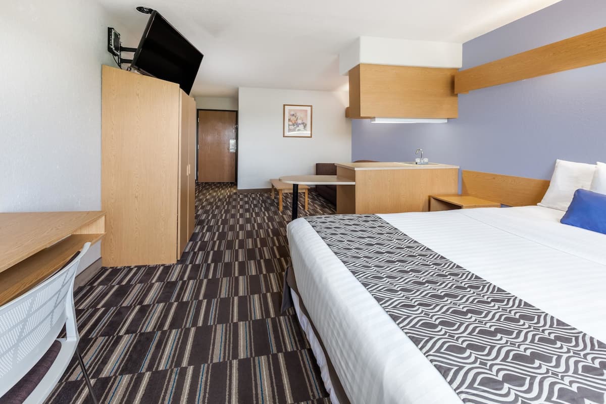 A hotel room with a bed, a desk, a chair, a wardrobe, and a television.