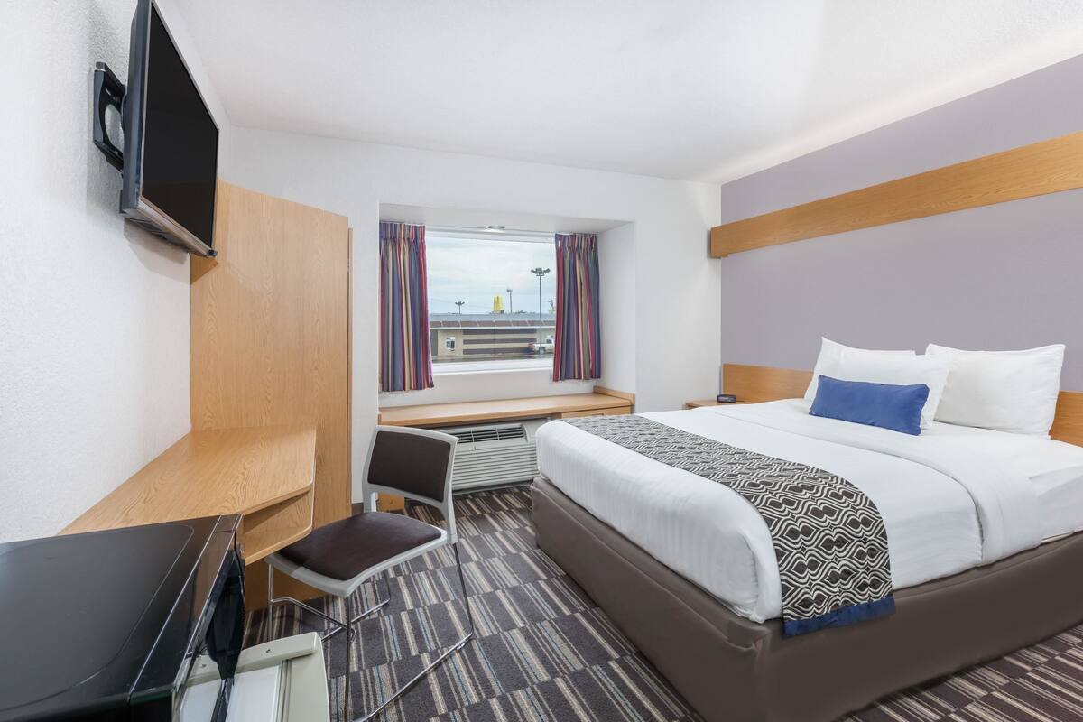 A hotel room with a bed, a desk, a chair, a TV, and a window with curtains.