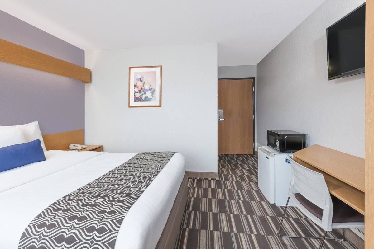 A hotel room with a bed, a desk with a microwave, a television, and a door leading to another room.