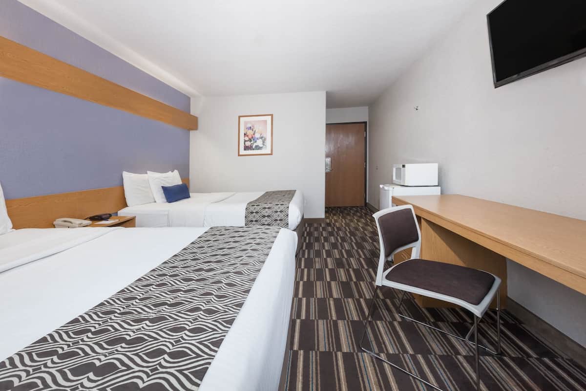 A hotel room with two beds, a desk, a chair, a microwave, and a door.