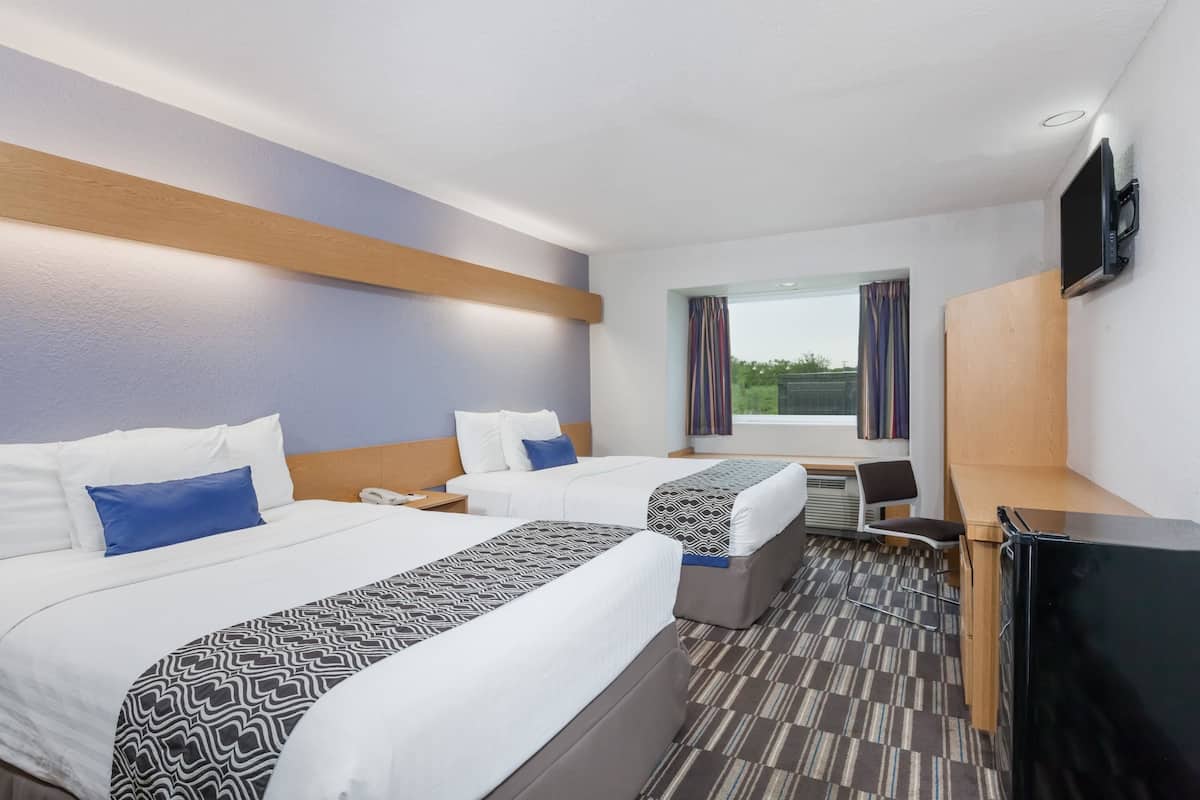 A hotel room with two beds, a desk, a TV, and a window with curtains.