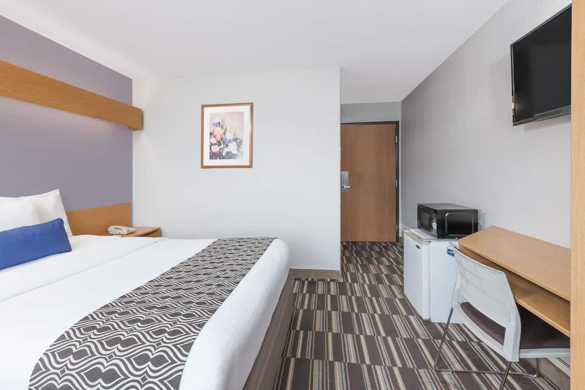 A hotel room with a bed, a desk, a microwave, a TV, and a door leading to another room.