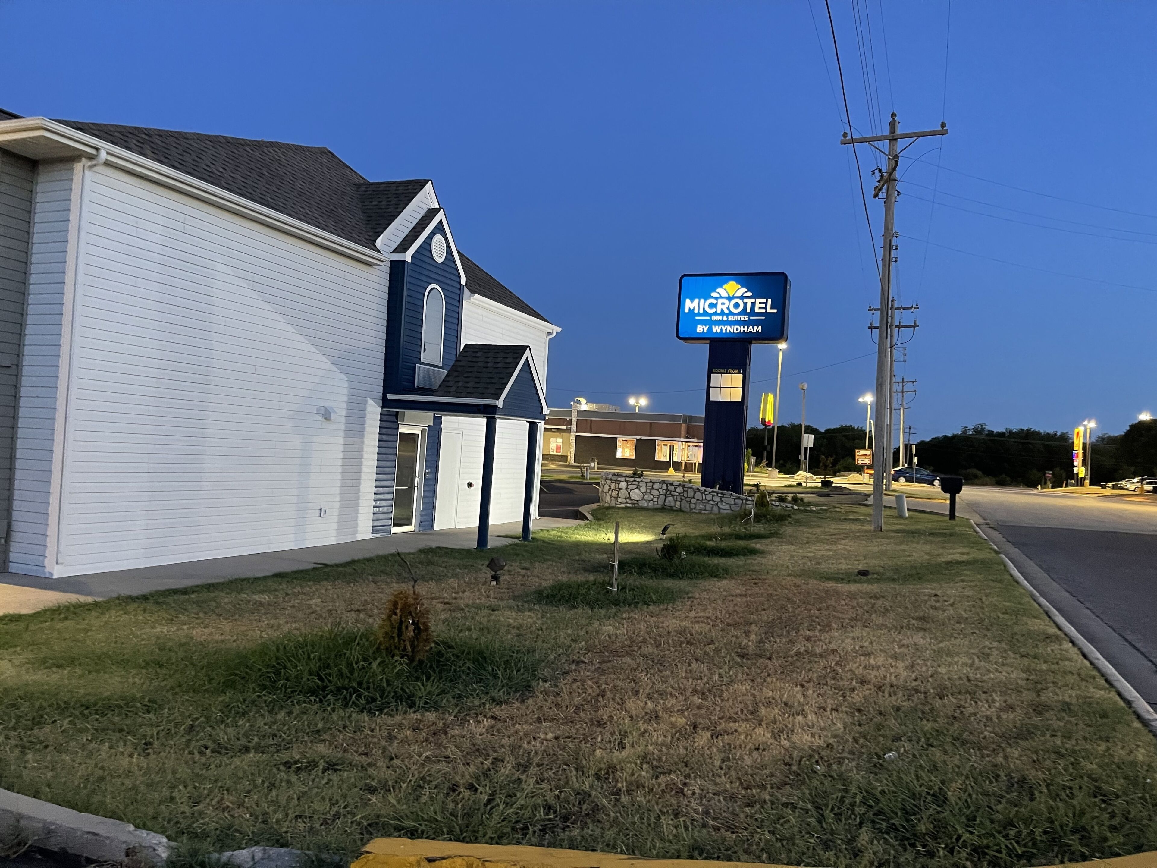 A Microtel Inn & Suites by Wyndham with a white exterior and a blue roof, located near a road with a McDonald's sign in the background.