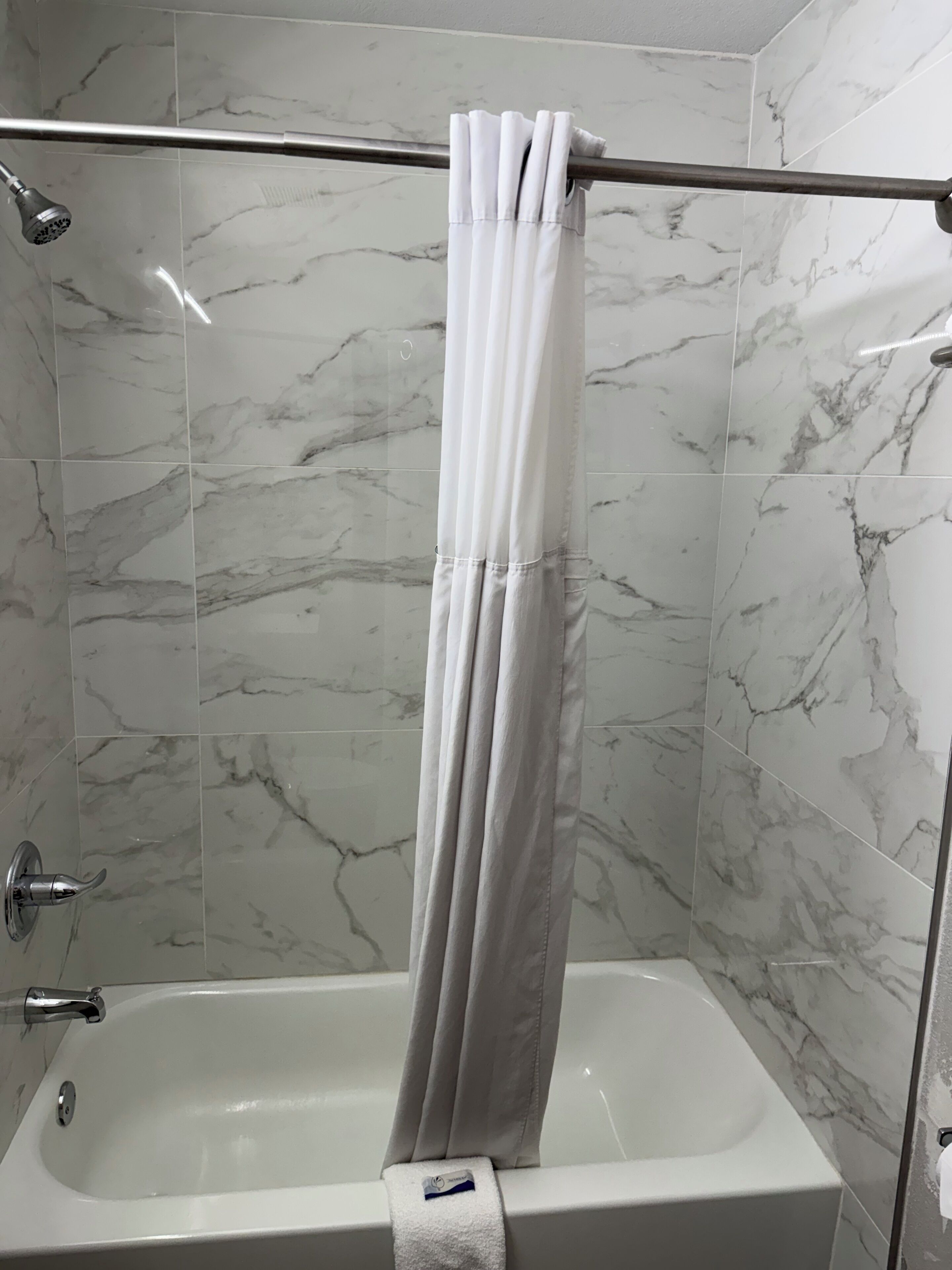A bathroom with a shower curtain, a bathtub, and marble tiles.