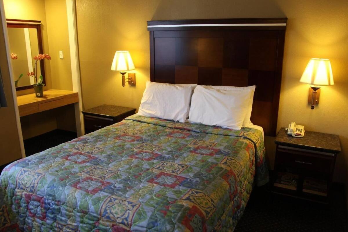 Ein Hotelzimmer mit einem großen Bett, zwei Nachttischen, einem Spiegel und zwei Wandleuchten.