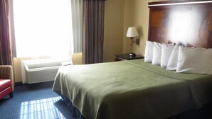 A hotel room with a large bed, a nightstand, a lamp, a chair, and a window with curtains. - Inn@Bayshore (San Mateo)