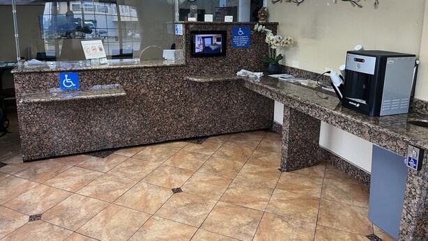 A reception area with a granite counter, a clock, a security camera, and a coffee machine. - Inn@Bayshore (San Mateo)