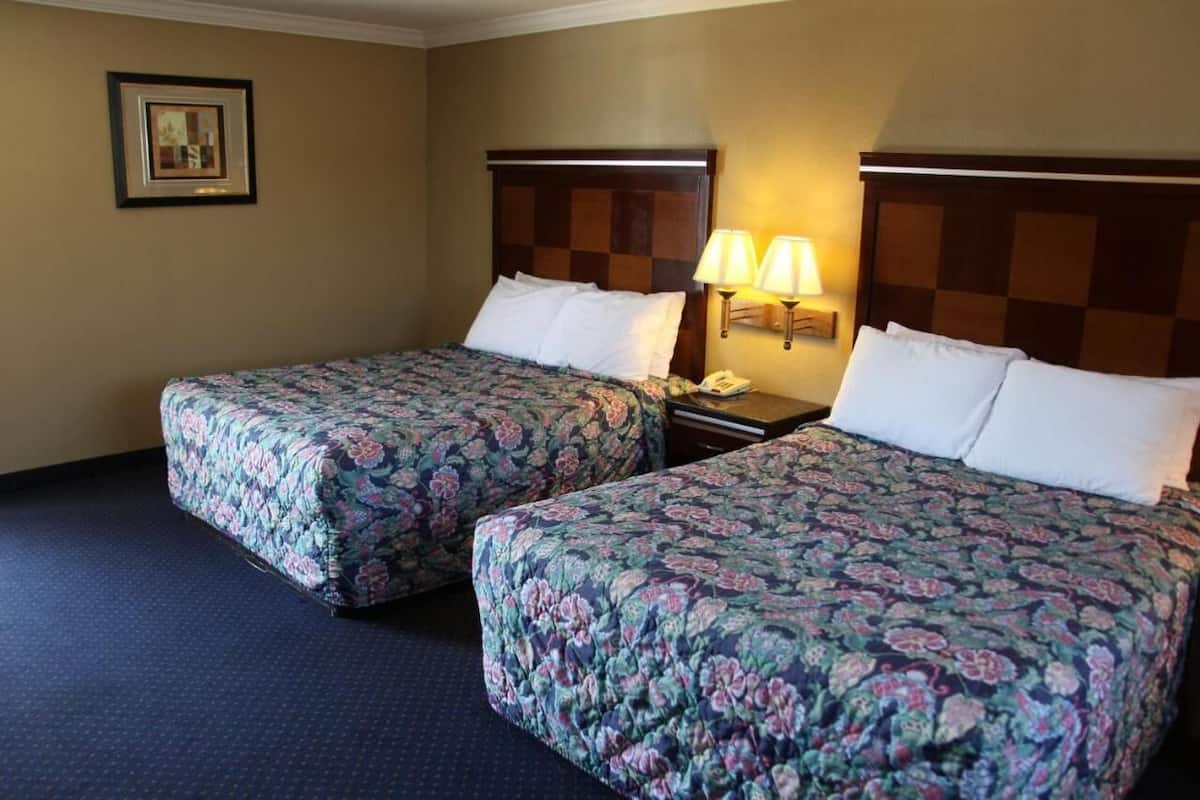 Ein Hotelzimmer mit zwei Betten, jedes mit blumigem Bettbezug, einem Nachttisch mit Lampe und einem gerahmten Bild an der Wand.