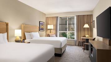 Quarto de hotel com duas camas, uma escrivaninha, televisão e janela com cortinas.
