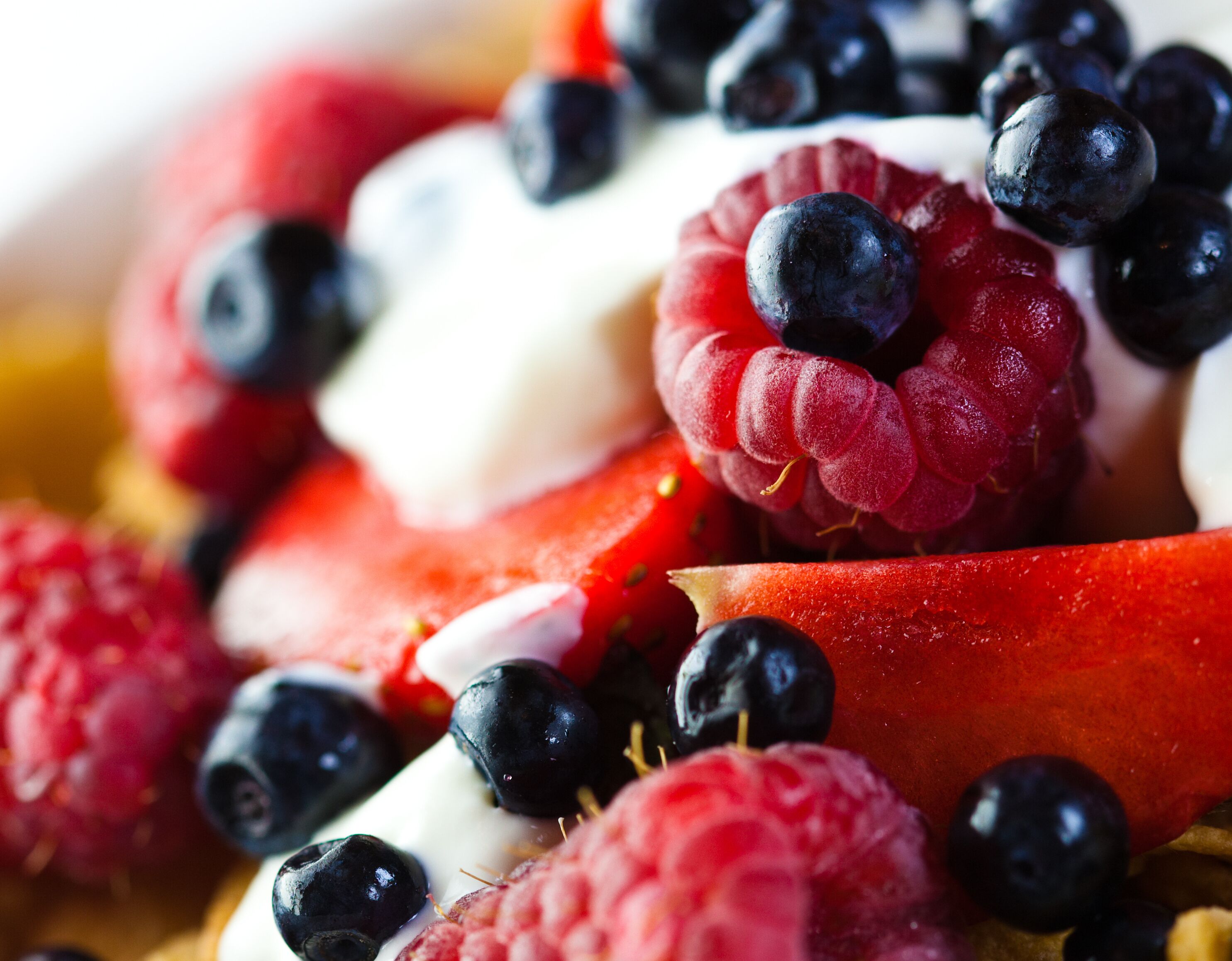 Een close-up van verschillende soorten fruit, zoals frambozen, bosbessen en plakjes appel.