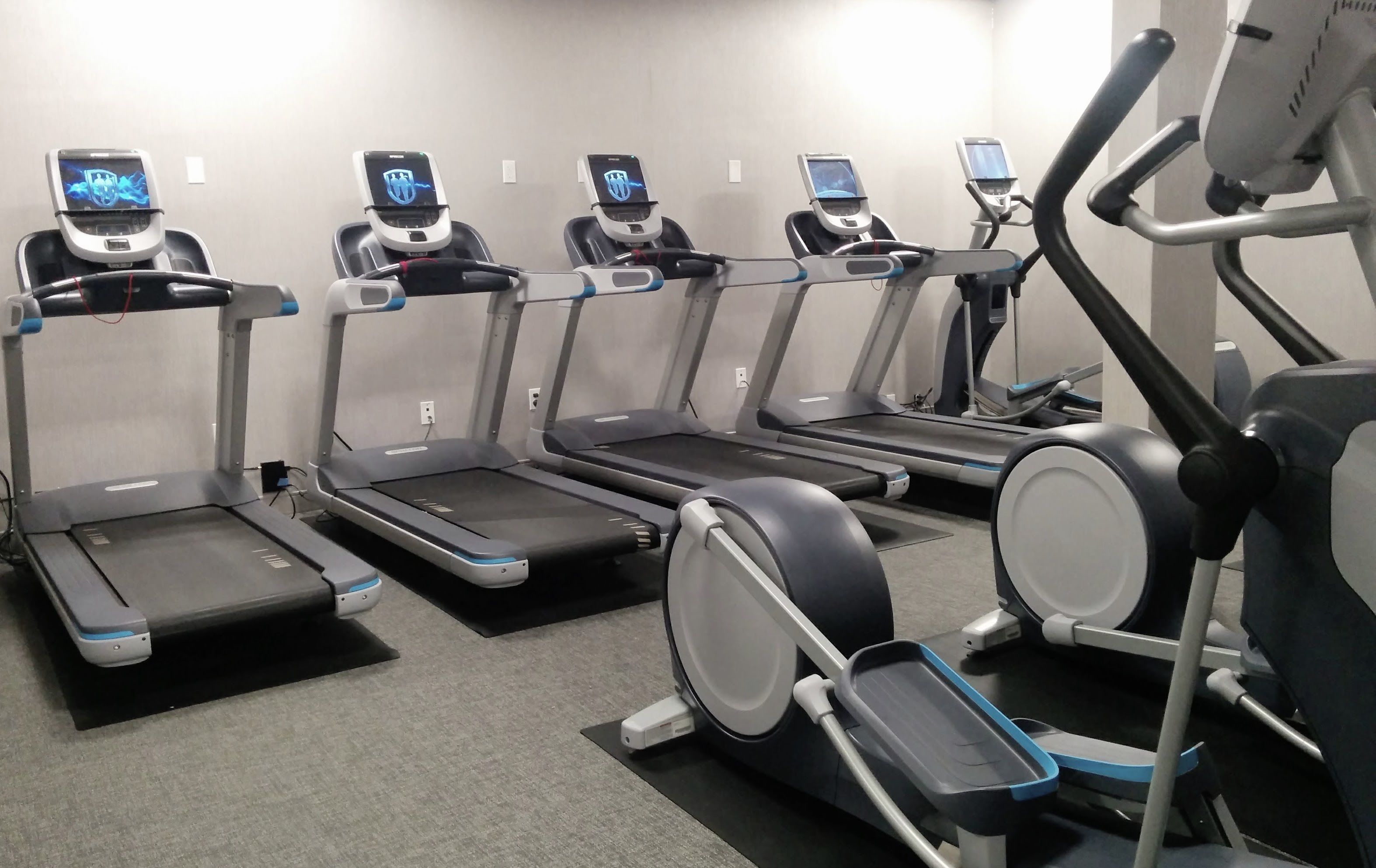 A row of treadmills with digital screens, each equipped with a handlebar and a foot platform.
