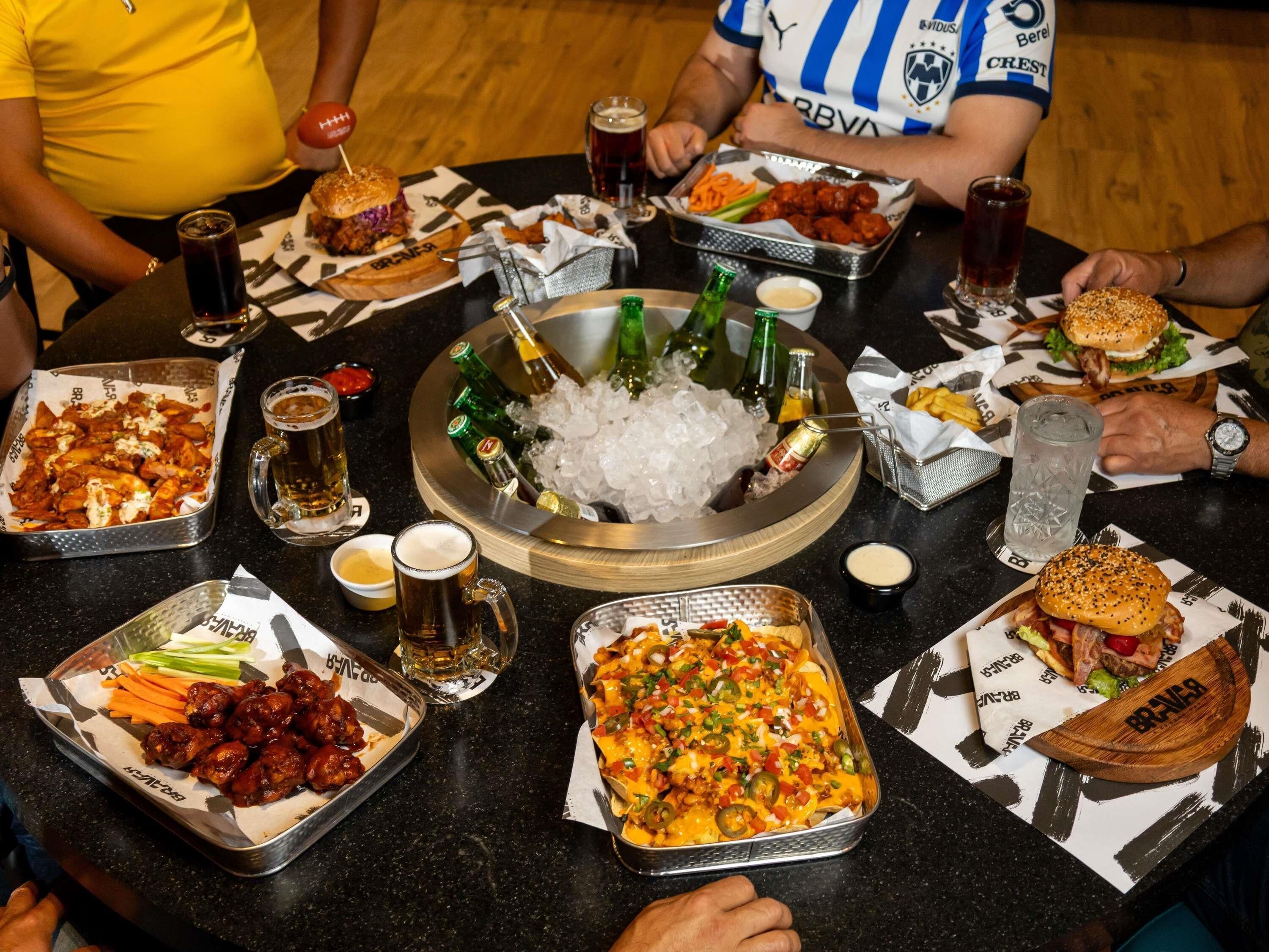 Una mesa de comedor con diversas opciones de comida, bebidas y un centro de mesa con hielo y botellas.