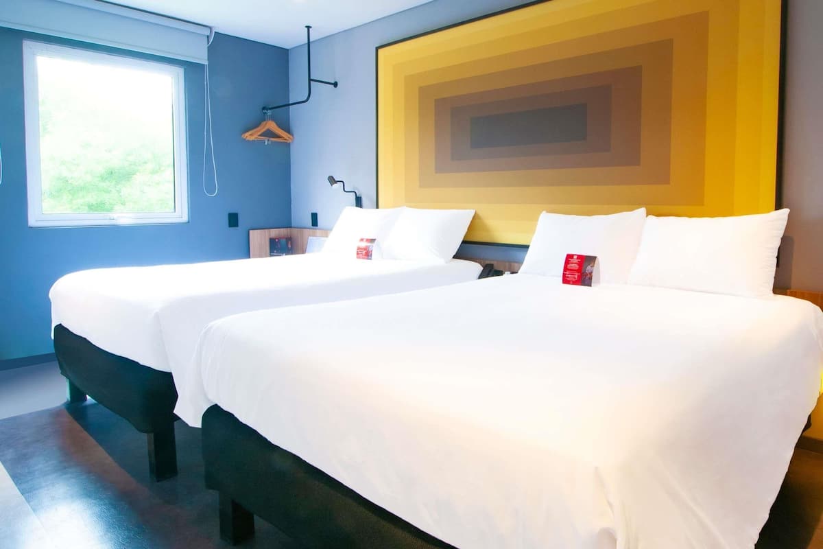 Habitación de hotel con dos camas, un ventanal grande y un diseño moderno en la pared.