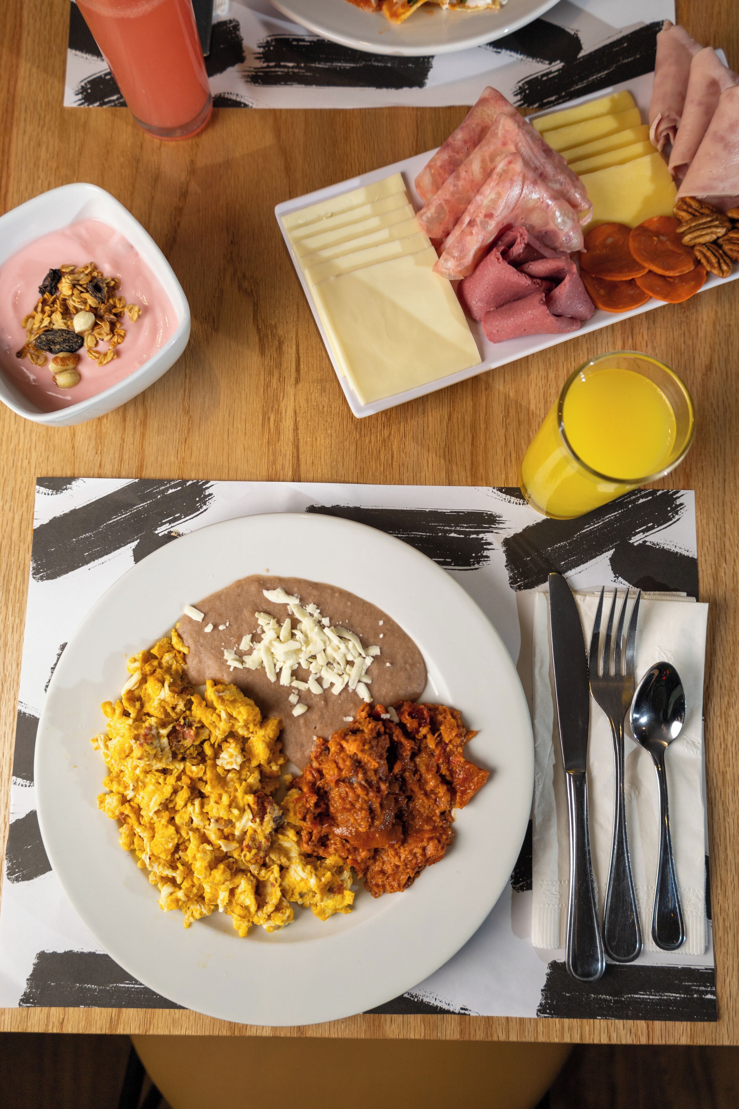 A breakfast plate with scrambled eggs, refried beans, and a side of refried beans with cheese.