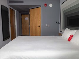 Una habitación de hotel con cama, ventana, puerta y una lámpara fijada a la pared.