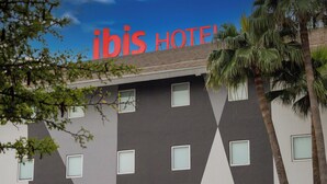 Un hotel de diseño moderno, con un llamativo letrero 'ibis HOTEL', varias ventanas y palmeras.
