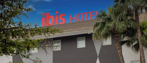 Un hotel de diseño moderno, con un llamativo letrero 'ibis HOTEL', varias ventanas y palmeras.
