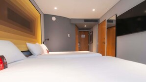Habitación de hotel con dos camas, un televisor de pantalla plana montado en la pared y una puerta que da a otra habitación.