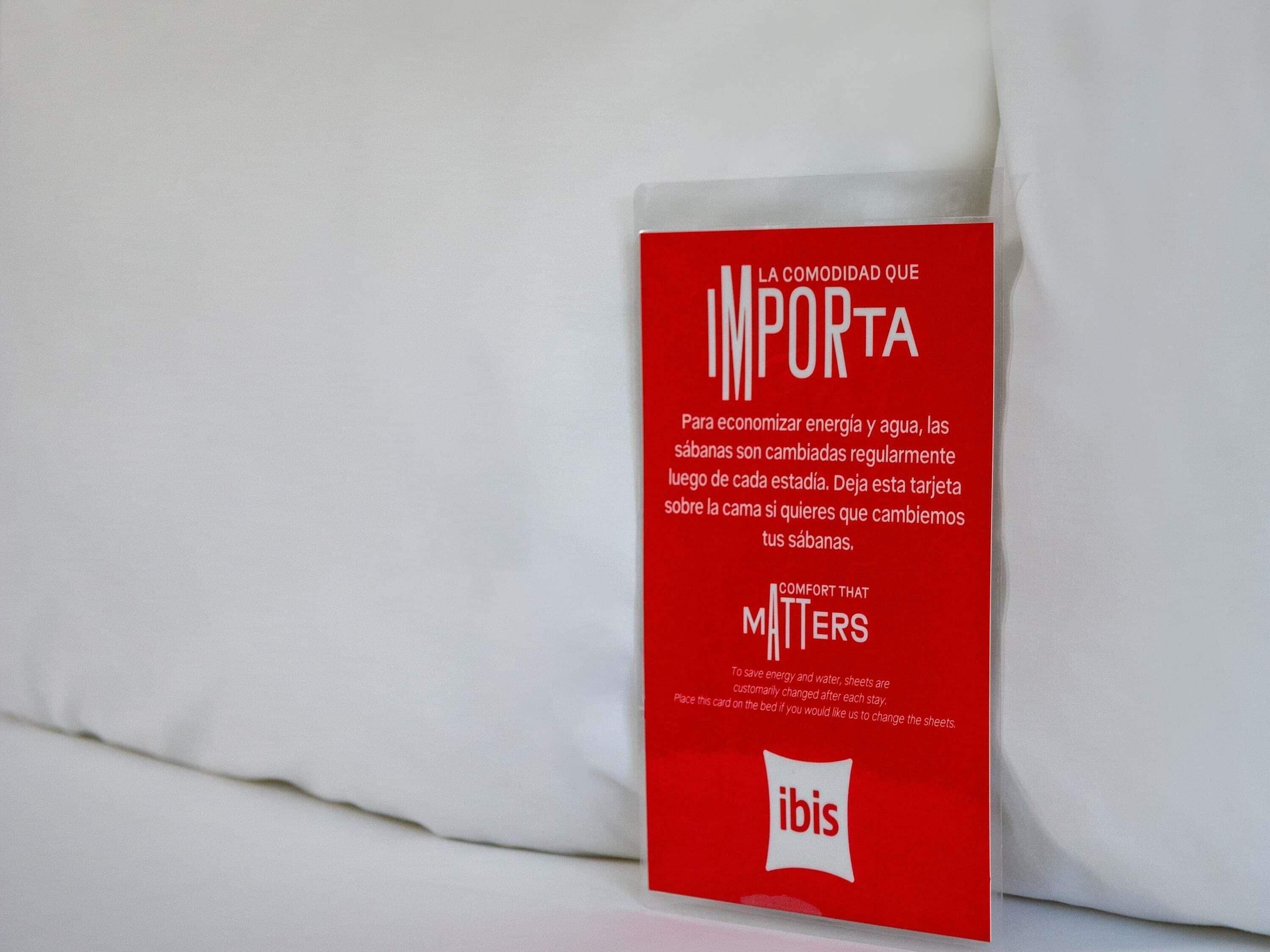 A red card with text in Spanish and English, placed on a white surface, likely a bed.