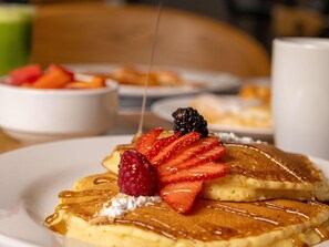 A plate of pancakes with syrup, strawberries, and a blackberry on top. - ibis Monterrey Aeropuerto (Apodaca)
