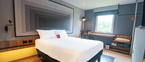 A modern hotel room with a large bed, a desk with a chair, a window with a view of trees, and a large abstract painting on the wall.