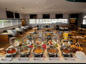 Ein Buffetbereich mit verschiedenen Speiseauslagen, Sitzgelegenheiten und großen Fenstern für natürliches Licht.