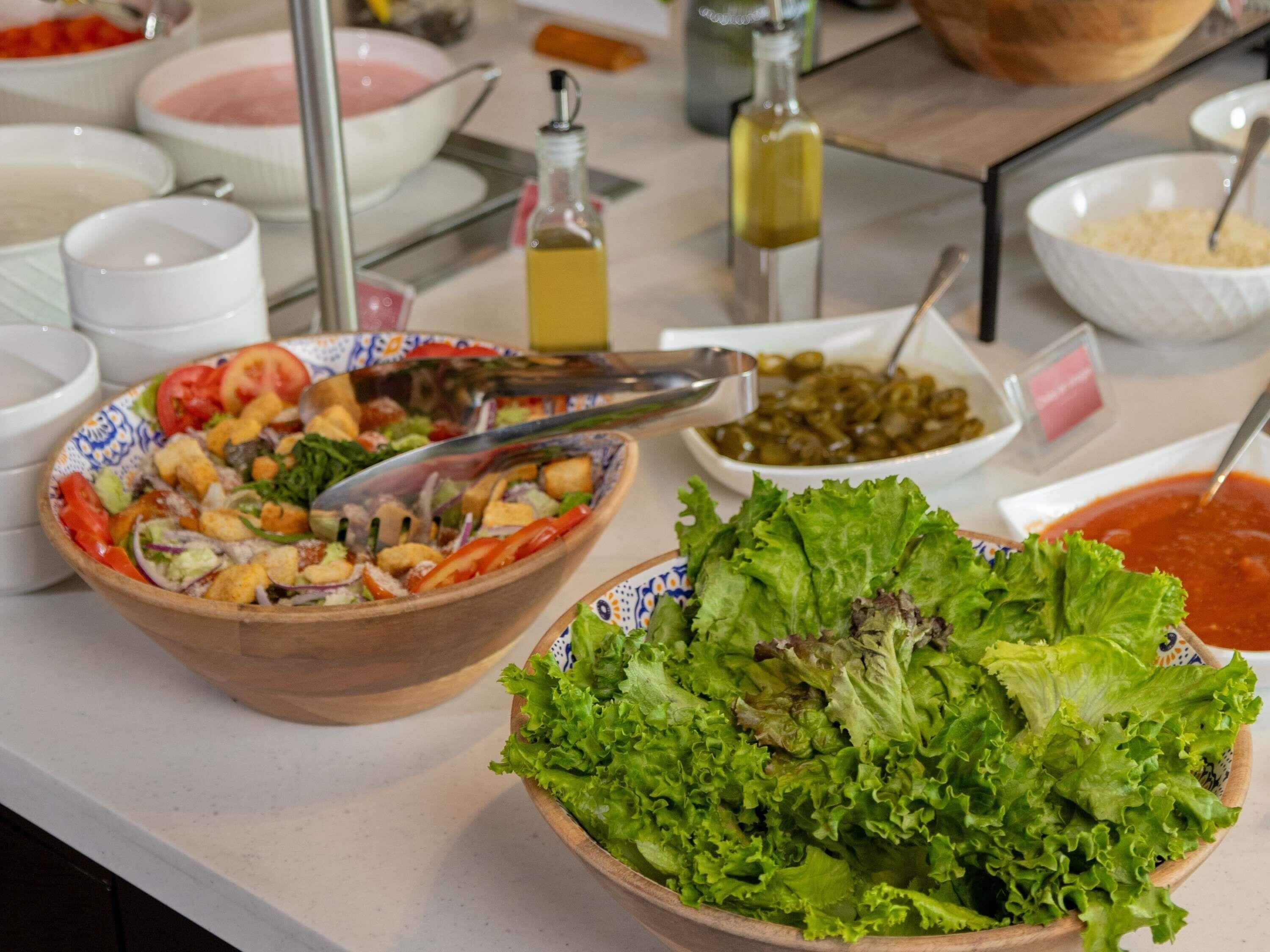 A buffet table with various dishes including a salad, a bowl of lettuce, and several small bowls with different condiments.