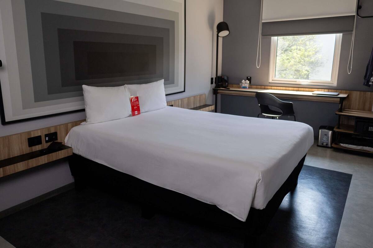 Una habitación de hotel moderna con una cama grande, un escritorio, una silla y un ventanal.