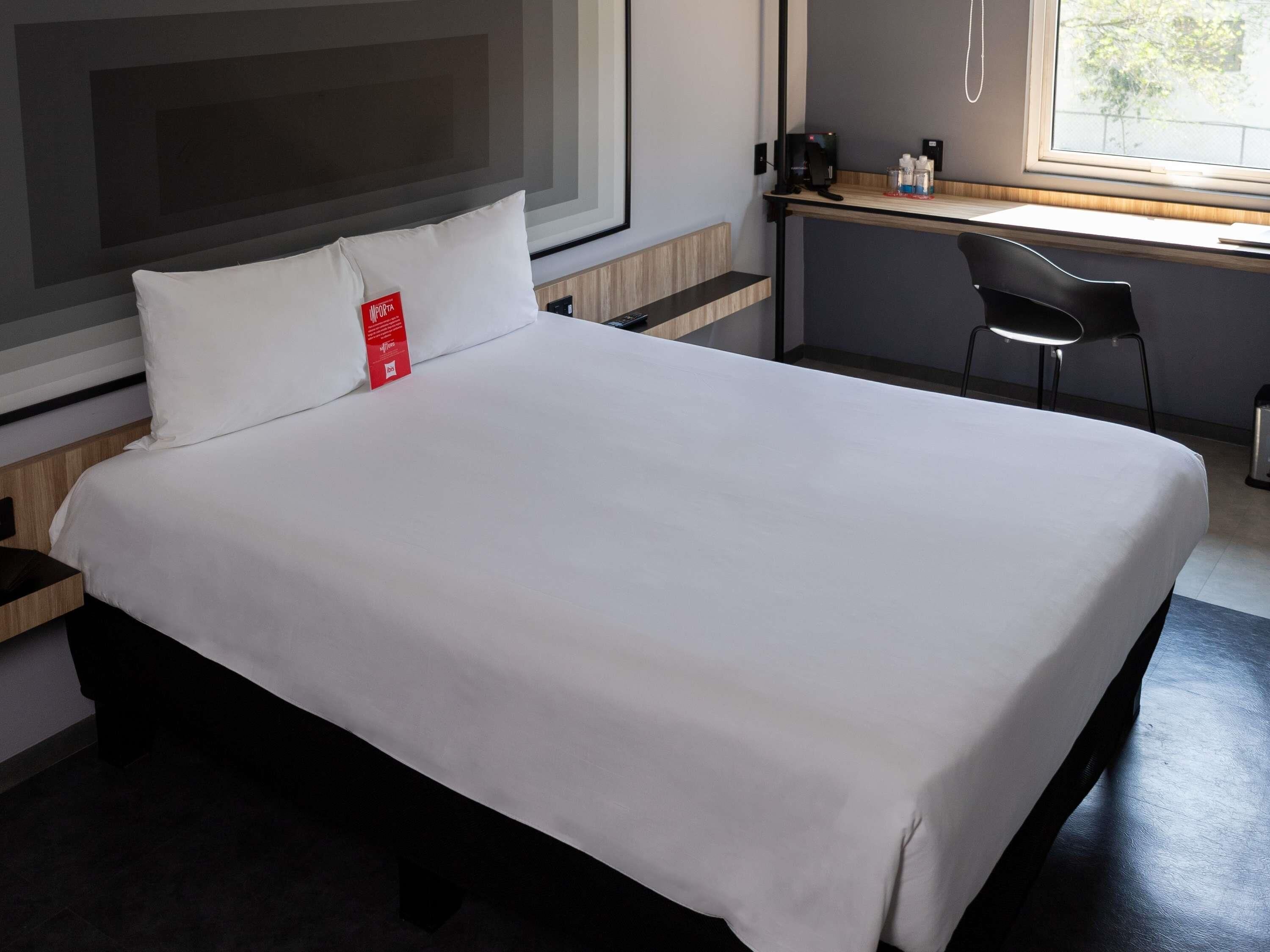 A hotel room with a bed, a desk, a chair, and a window.
