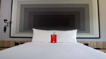 A hotel room with a large framed artwork on the wall, a white bed with a pillow, and a red tag on the pillow.