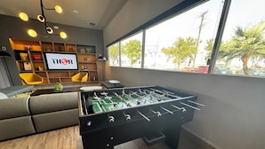 Una habitación moderna con una mesa de fútbol, un sofá, un televisor y una estantería.