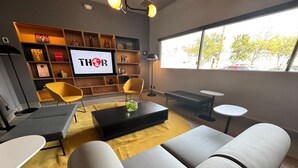 Una sala de estar moderna con un sofá, una mesa de centro y sillas. Hay un televisor en la pared y una estantería con varios objetos.