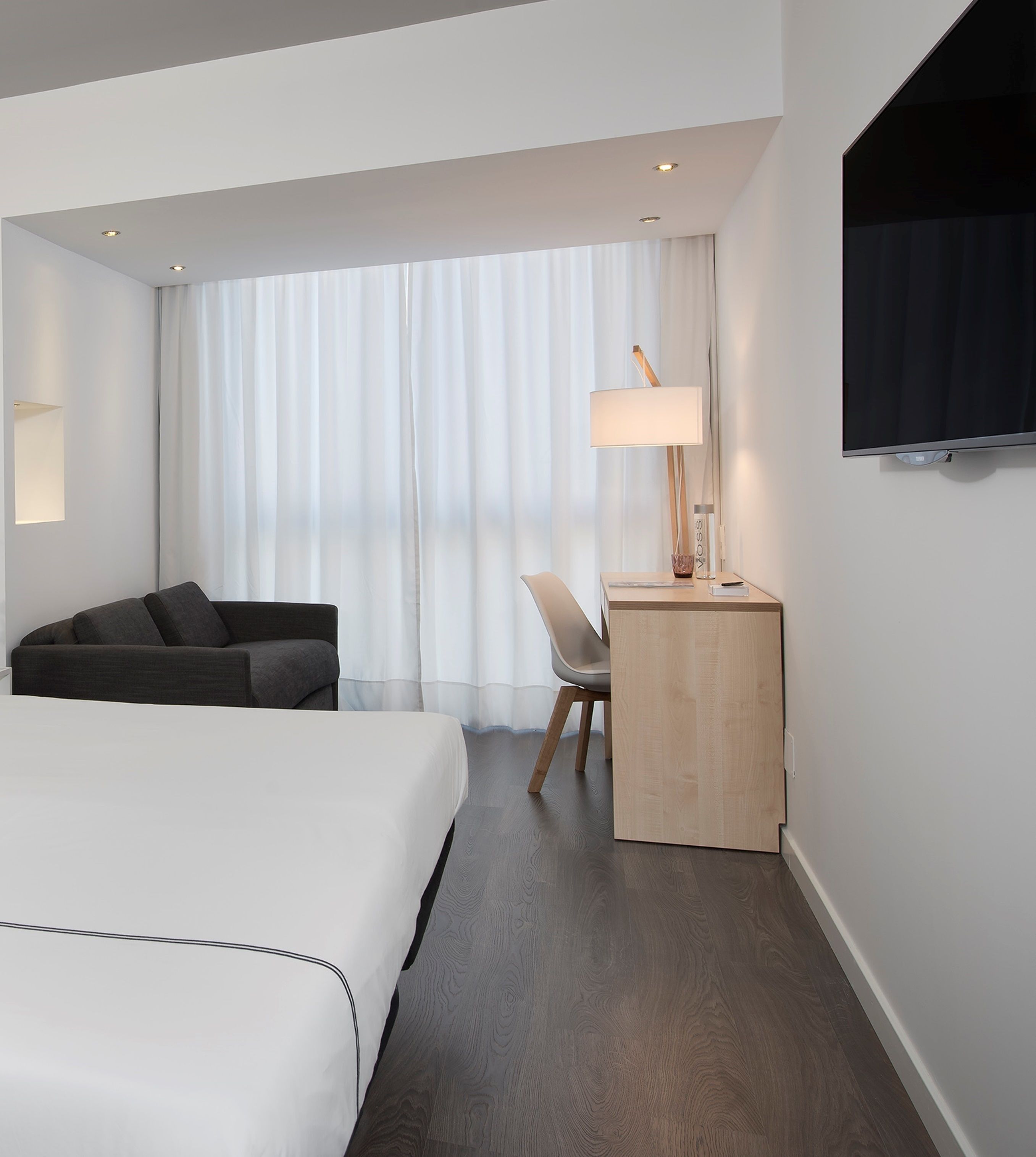 Habitación de hotel con cama, escritorio, silla, lámpara y televisor en la pared.