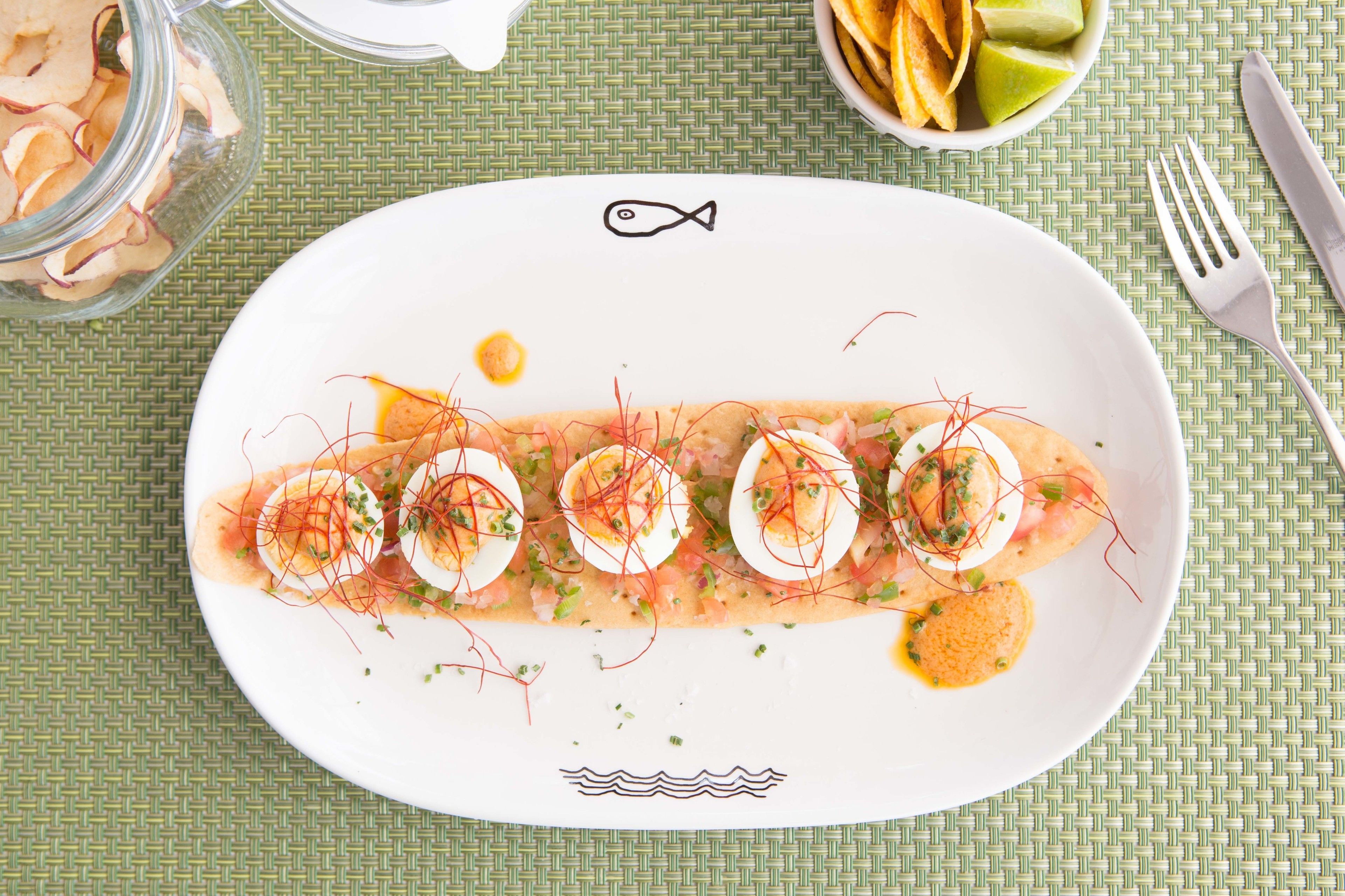 Un plato blanco con un símbolo de pescado, que contiene un plato con huevos, verduras y salsa.