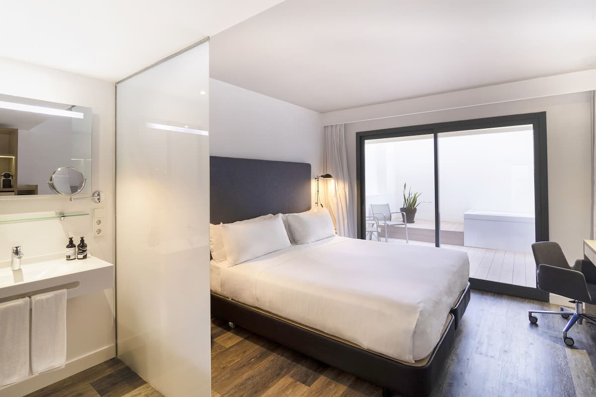 Ein modernes Hotelzimmer mit einem großen Bett, einem Badezimmer mit einer Duschkabine aus Glas, einem Schreibtisch und Blick ins Freie.