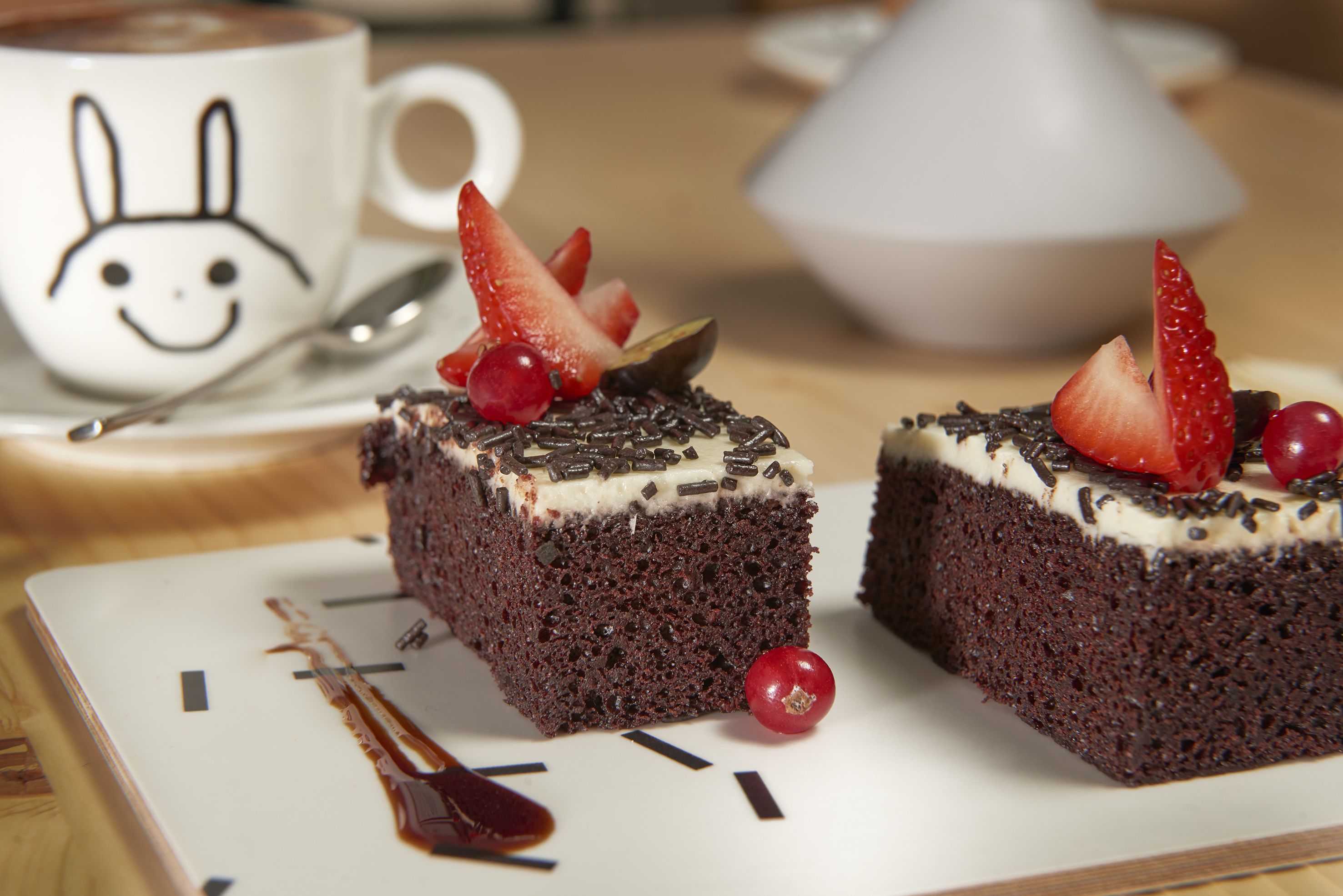 Two square chocolate cakes with white frosting and red berries on a white plate.