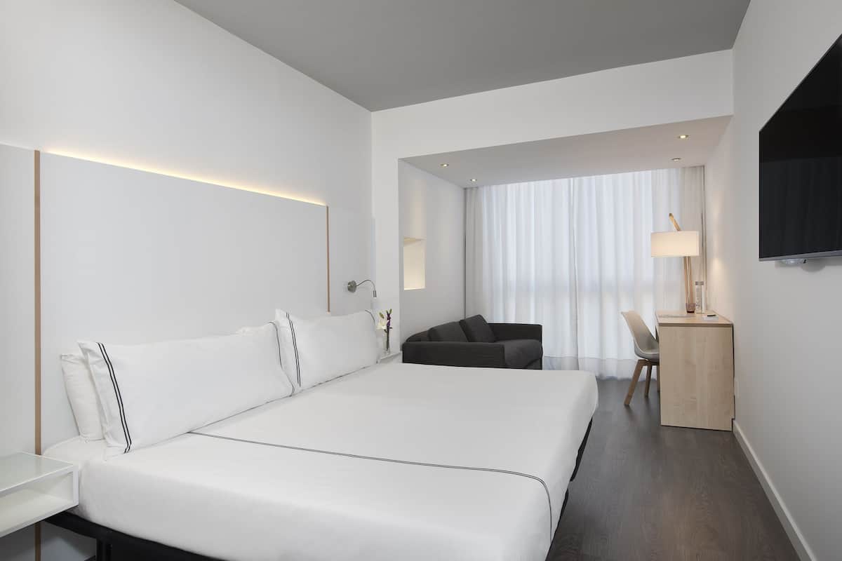 Ein modernes Hotelzimmer mit einem großen Bett, einem Schreibtisch, einem Stuhl und einem Fernseher.
