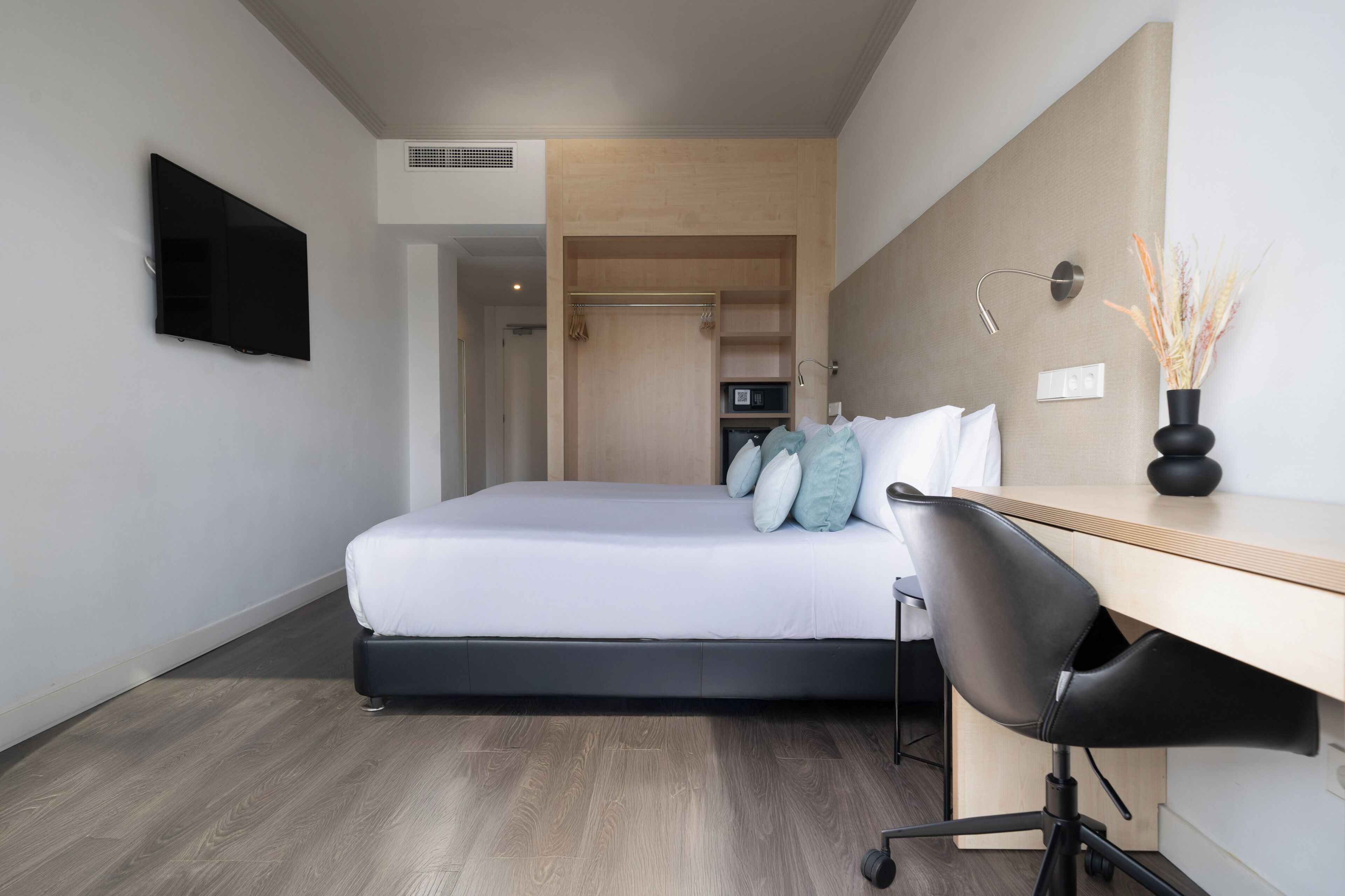 Una habitación de hotel moderna con cama, escritorio, silla, televisor y armario.