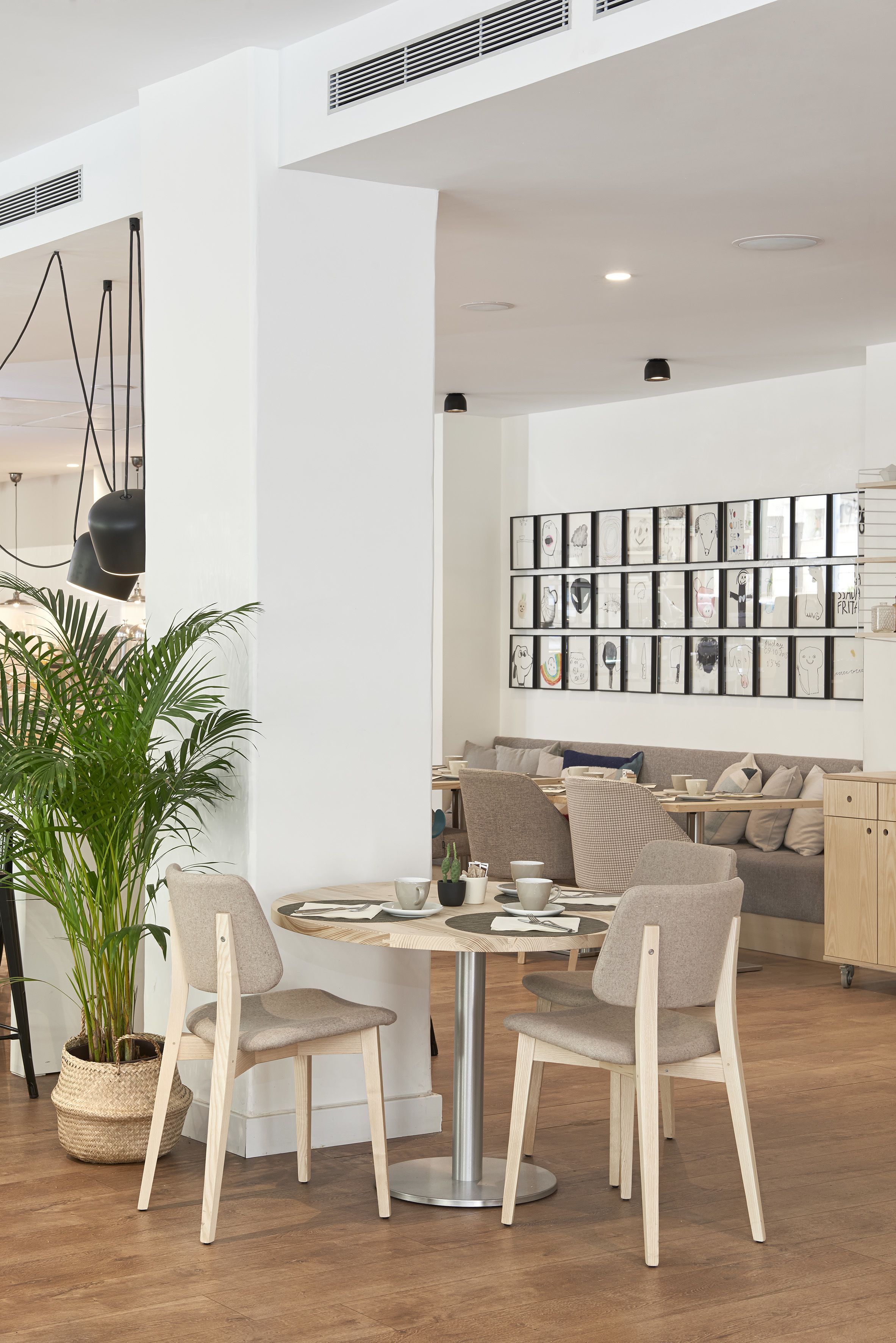A modern dining area with a round table, two chairs, a potted plant, and a wall of framed artwork.
