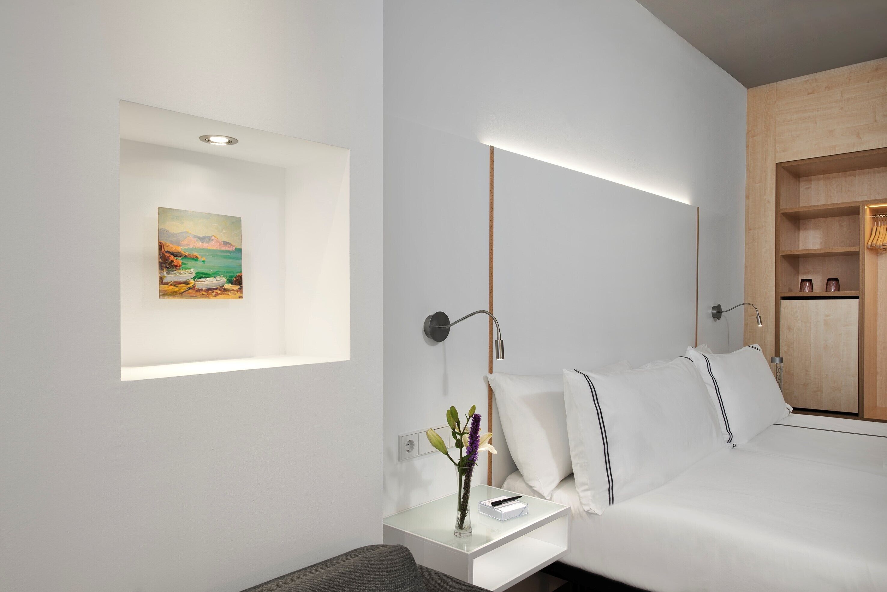 A modern hotel room with a bed, bedside table, and a painting on the wall.