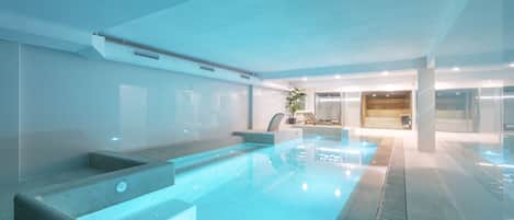 Una piscina interior moderna con agua cristalina, una zona de estar y un mostrador de recepción.